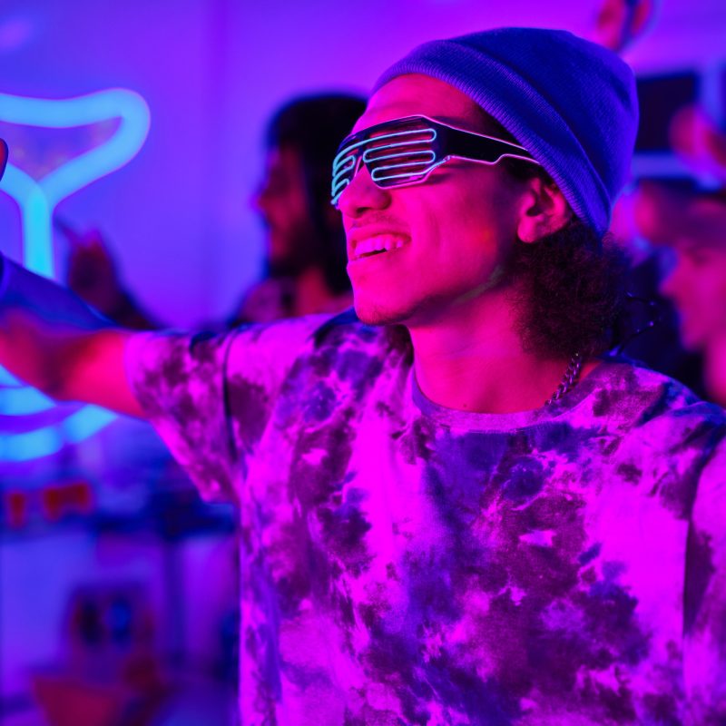 Young smiling man in neon eyeglasses and casualwear dancing at party